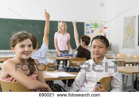 Stock Image - Two pre-adolescent girls sitting in the back of a classroom, looking at camera. Fotosearch