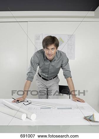 An architect leaning over blueprints on a desk View Large Photo Image Stock Photo - An architect leaning over blueprints on a desk. Fotosearch
