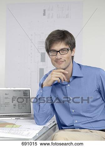 An architect sitting at his desk with a laptop and architectural drawings View Large Photo Image Stock Photography - An architect sitting at his desk with a laptop and architectural drawings. Fotosearch