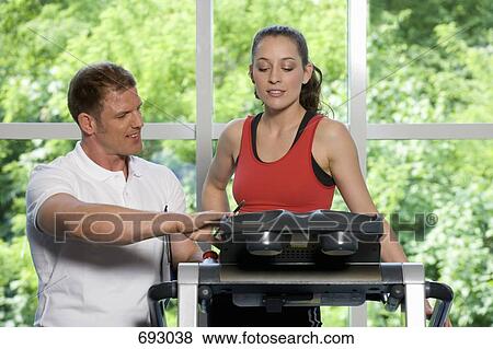 Stock Photo - A fitness instructor helping a young woman on a treadmill. Fotosearch