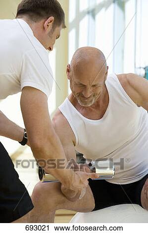 Stock Image - A man lifting a weights with a personal trainer. Fotosearch