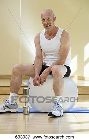Stock Photo - A man resting on an exercise ball with a dumbbell next to him. Fotosearch