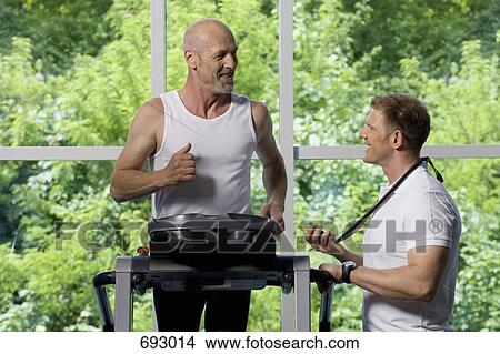 A man running on a treadmill and being timed by a personal trainer View Large Photo Image Picture - A man running on a treadmill and being timed by a personal trainer. Fotosearch