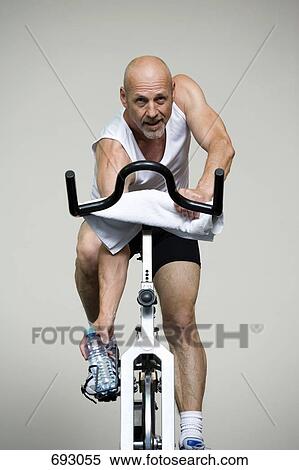 A mature man on a stationary bike reaching for a water bottle View Large Photo Image Stock Photography - A mature man on a stationary bike reaching for a water bottle. Fotosearch