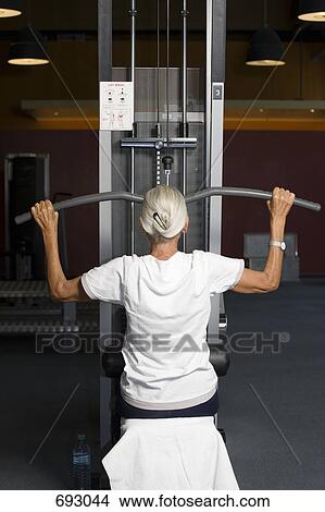 A senior woman using a lateral pull-down weight machine View Large Photo Image Picture - A senior woman using a lateral pull-down weight machine. Fotosearch