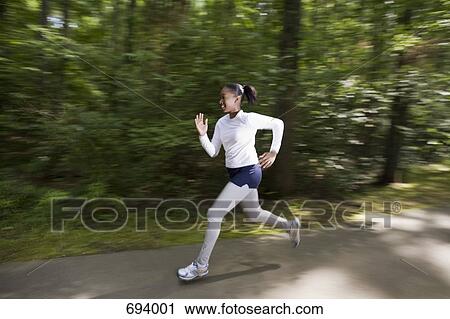 Stock Image - A woman jogging through a wooded park. Fotosearch