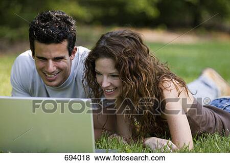 A young couple lying on their fronts looking at a laptop and laughing View Large Photo Image Stock Photo - A young couple lying on their fronts looking at a laptop and laughing. Fotosearch