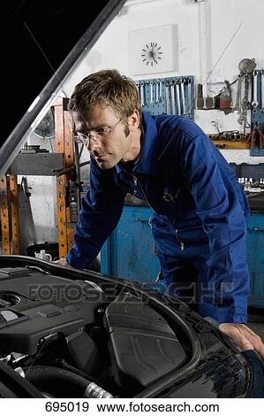 Stock Photo - A car mechanic examining a car engine. Fotosearch