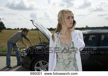 Stock Image - A couple standing at the roadside next to their broken down car. Fotosearch