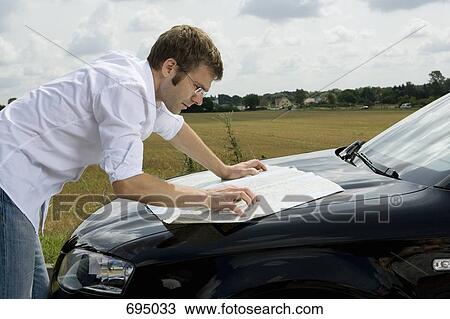Stock Image - A man leaning on a car bonnet and reading a map. Fotosearch