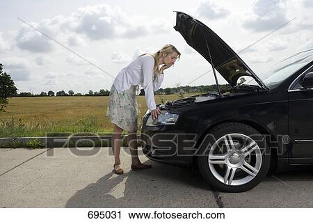 Stock Image - A woman leaning over an open bonnet at the roadside. Fotosearch
