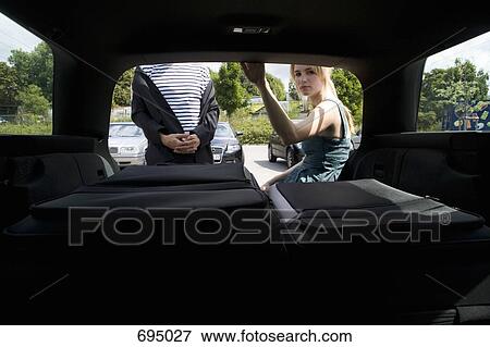 Stock Photo - A woman sitting at the boot of a car with suitcases. Fotosearch