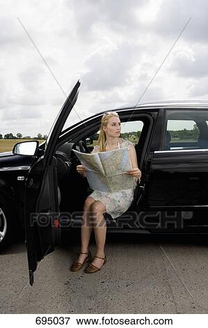 A woman sitting in a car with the door open and reading a map View Large Photo Image Stock Photo - A woman sitting in a car with the door open and reading a map. Fotosearch