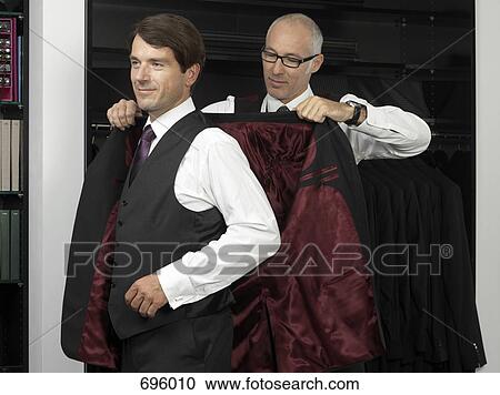 Stock Image - A tailor assisting a man trying on a suit. Fotosearch