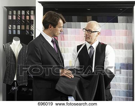 Stock Photo - A tailor showing a man fabric for a suit. Fotosearch