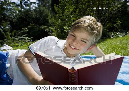 A boy lying on a blanket and reading a book View Large Photo Image Stock Image - A boy lying on a blanket and reading a book. Fotosearch