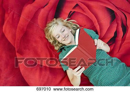 Stock Image - A girl lying on a blanket and reading a book. Fotosearch