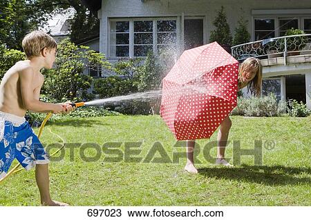 Stock Image - A young boy spraying at his sister with a garden hose. Fotosearch