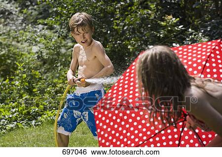 Stock Photograph - A young boy spraying at his sister with a garden hose. Fotosearch