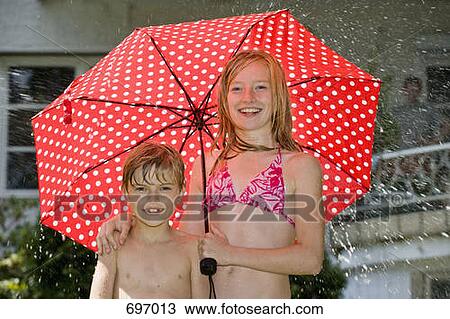 Stock Image - Two Children standing under an umbrella in their bathing suits. Fotosearch