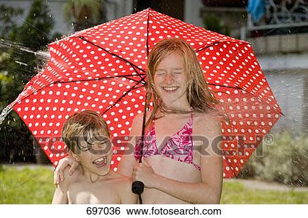 Stock Photograph - Two children standing under an umbrella and getting hit by spraying water. Fotosearch