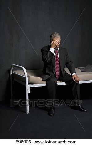 A business man sitting on a bed in a prison cell View Large Photo Image Stock Photograph - A business man sitting on a bed in a prison cell. Fotosearch