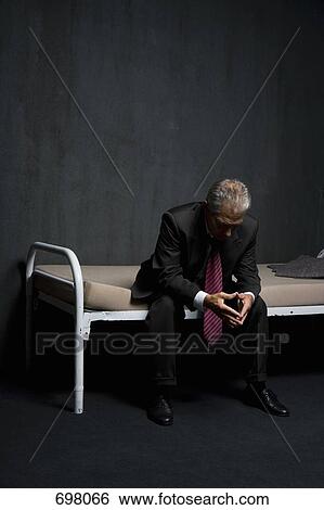 Stock Photograph - A business man sitting on a prison cell bed. Fotosearch