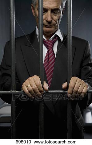 Stock Image - A business man standing behind prison cell bars. Fotosearch