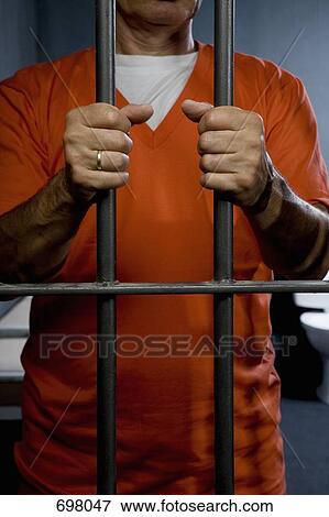 Stock Photo - A prisoner standing behind his prison cell door. Fotosearch