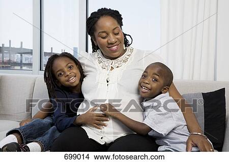 Picture - Two boys with their hands on their pregnant Mom's belly. Fotosearch