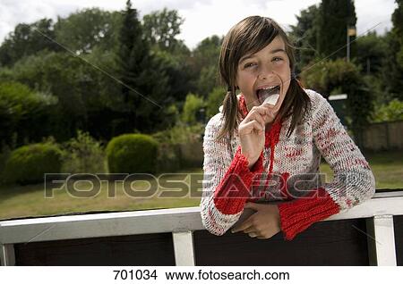A young girl leaning over a fence, eating an ice cream bar View Large Photo Image Picture - A young girl leaning over a fence, eating an ice cream bar. Fotosearch