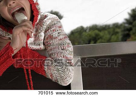 A young girl leaning over a fence, eating an ice cream bar View Large Photo Image Stock Photography - A young girl leaning over a fence, eating an ice cream bar. Fotosearch