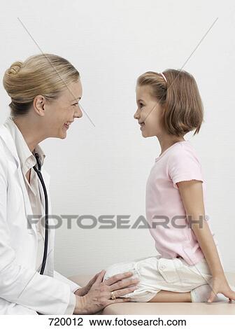 Stock Image - A girl on an exam table facing a pediatrician and smiling. Fotosearch
