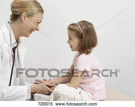 A girl on an exam table facing a pediatrician and smiling View Large Photo Image Stock Photography - A girl on an exam table facing a pediatrician and smiling. Fotosearch