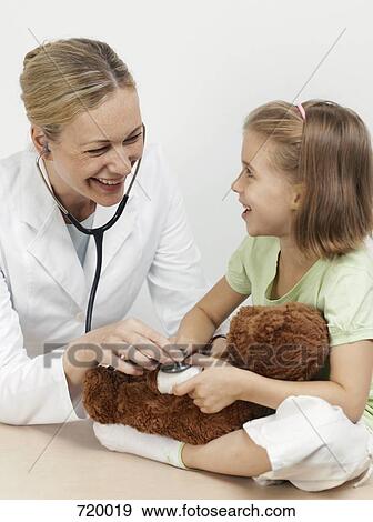 Stock Photo - Female pediatrician examining a girl's teddy bear. Fotosearch