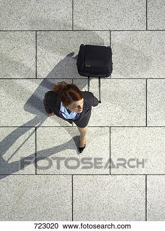 Stock Image - A businesswoman pulling a suitcase. Fotosearch