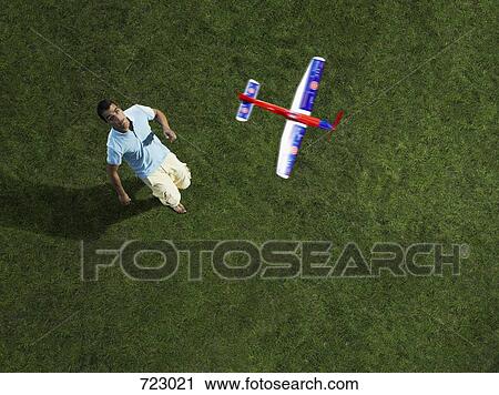 Stock Image - A man looking up at a toy airplane flying in the air. Fotosearch