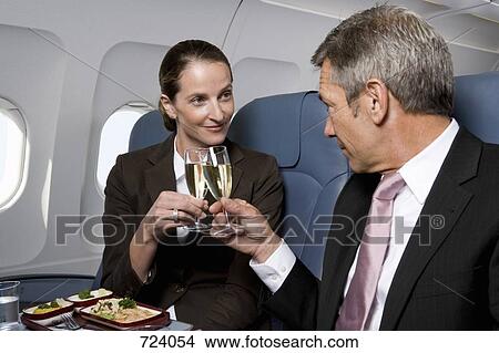 Picture - A businessman and a businesswoman toasting champagne glasses on a plane. Fotosearch