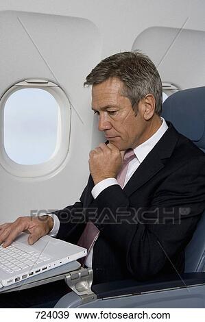 A businessman using a laptop on a plane View Large Photo Image Stock Photo - A businessman using a laptop on a plane. Fotosearch