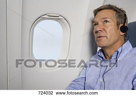 A male passenger listening to headphones on a plane View Large Photo Image Stock Image - A male passenger listening to headphones on a plane. Fotosearch