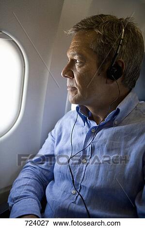 A male passenger listening to headphones and looking out the window of a plane View Large Photo Image Stock Photo - A male passenger listening to headphones and looking out the window of a plane. Fotosearch