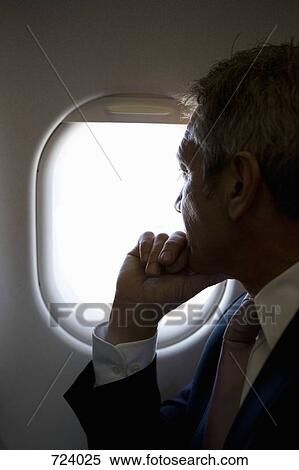 A male passenger looking through a window on a plane View Large Photo Image Stock Photography - A male passenger looking through a window on a plane. Fotosearch