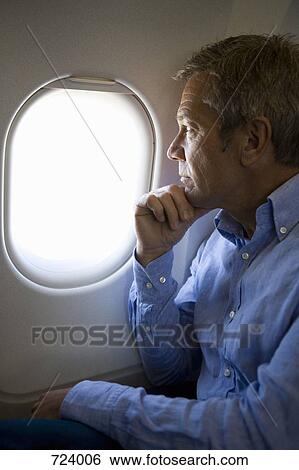 A male passenger on a plane looking through window View Large Photo Image Stock Photograph - A male passenger on a plane looking through window. Fotosearch