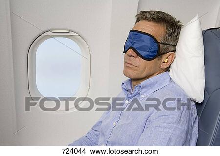 A man wearing a sleep mask sleeping on a plane View Large Photo Image Picture - A man wearing a sleep mask sleeping on a plane. Fotosearch