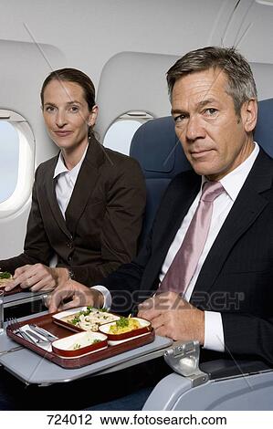 Stock Image - Business people eating on a plane. Fotosearch