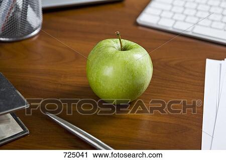 Stock Image - A green apple on an office desk. Fotosearch