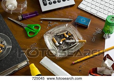 Stock Photography - An office desk cluttered with office supplies and ashtrays. Fotosearch