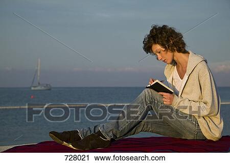 A woman sitting near the sea writing in a journal View Large Photo Image Stock Image - A woman sitting near the sea writing in a journal. Fotosearch