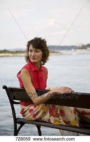 A woman sitting on a bench by the sea View Large Photo Image Stock Photo - A woman sitting on a bench by the sea. Fotosearch