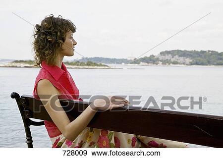 A woman sitting on a bench looking out at the sea View Large Photo Image Stock Photo - A woman sitting on a bench looking out at the sea. Fotosearch